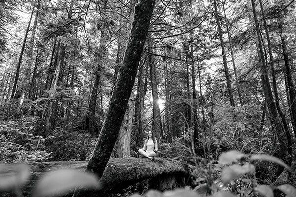 Laura meditating in the forest with trees all around her Tofino Breath & Meditation
